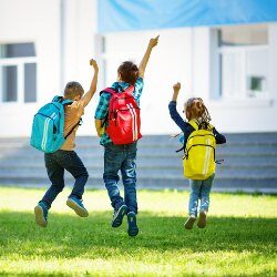 Students with colourful backpacks jump with their hands in the air