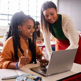 A teacher is helping a student working at a laptop