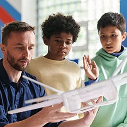 Male teacher holding model aeroplane with two young students