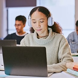 Female student using laptop wearing headphones. 