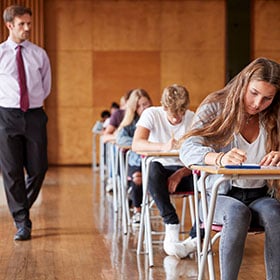 Teenage students sitting exam with male teacher invigilating.