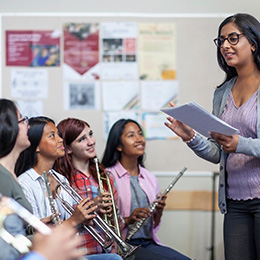 Female teacher talks to a group of students who are all holding musical instruments