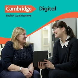 Two students smile at each other while chatting. One is holding a tablet.