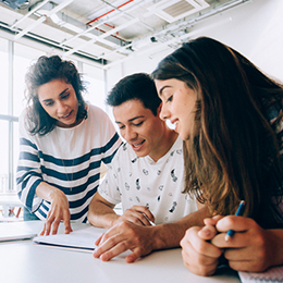 A group of three young adult students looking at a notebook